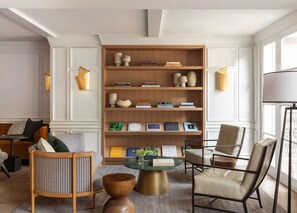 Een moderne woonkamer met een grote houten boekenkast, leren fauteuils, een ronde salontafel en een vloerlamp.
