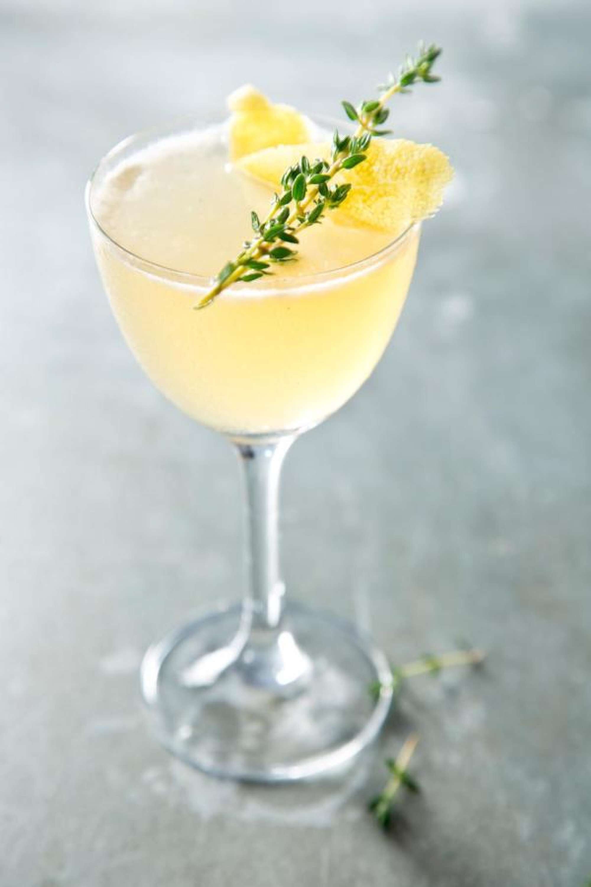 Cocktail-drinkki korkeassa lasissa, koristeltuna sitruunaviipaleella ja timjaminoksalla.