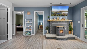 Una sala de estar con chimenea, televisor montado y estantería.