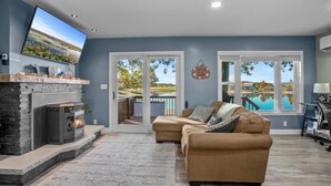 Una sala de estar con chimenea, un televisor de pantalla plana grande, un sofá y vistas a una piscina a través de amplios ventanales.