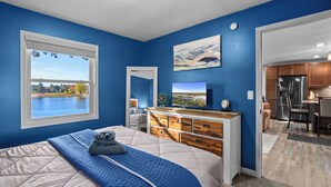 A bedroom with a large bed, a dresser, a TV, and a window overlooking a lake. - StoneLedge Lake Sauna&Spa
Cozy 2-Bed, 1-Bath lakeside retreat on StoneLedge Lake (Cadillac)