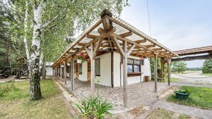 Katettu ulkoalue, jossa on puinen pergola, ruukussa oleva kasvi ja kivestä tehty polku, joka johtaa rakennukseen.