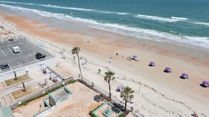 A beach with a parking area, palm trees, and beach umbrellas. - Oceanfront •Private Balcony •Overlooks Heated Pool (Daytona Beach)