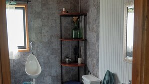 Une salle de bain comprenant des toilettes, un bidet et un lavabo, avec un plafond en bois, des murs carrelés et une fenêtre.