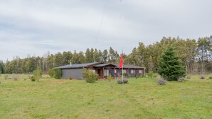 Une maison de plain-pied, à l’extérieur gris, avec un drapeau rouge flottant devant.