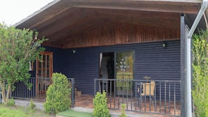 Une cabane en bois dotée d’un porche couvert, d’une porte et d’un petit espace extérieur aménagé pour s’asseoir.