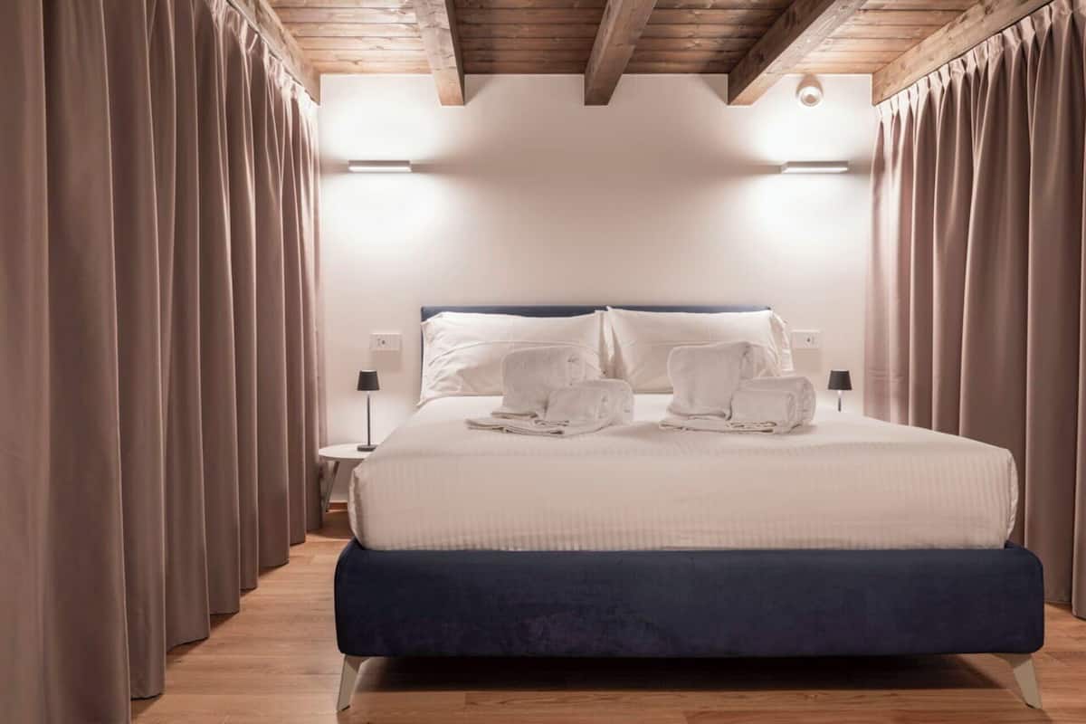 A modern hotel room with a large bed, two bedside lamps, and a wooden ceiling.
