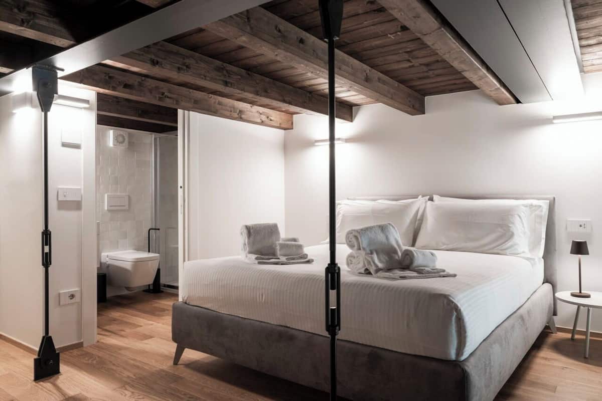 A modern bedroom with a large bed, a separate bathroom, and a wooden ceiling.