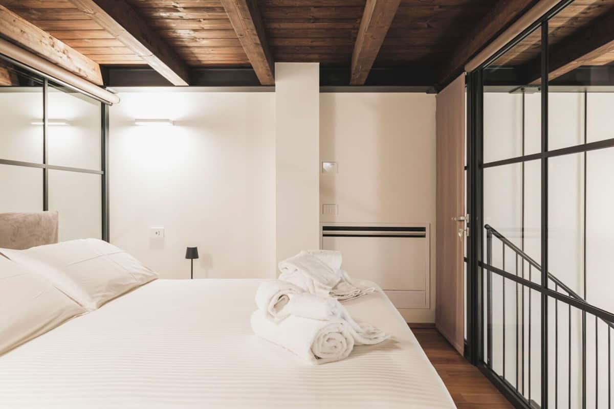 A hotel room with a bed, a wooden ceiling, a sliding glass door, and a small table with towels.