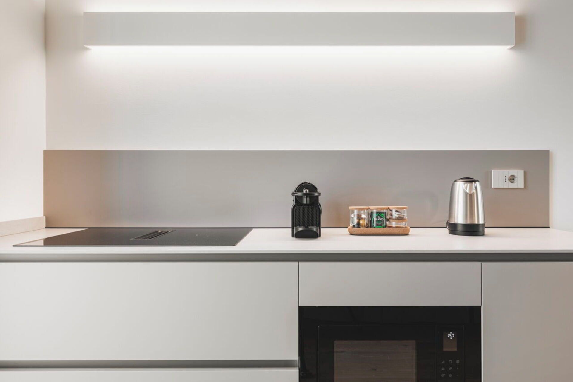 A modern kitchen with a built-in stove, a coffee maker, and a kettle on the countertop.