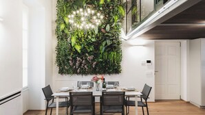 A dining area with a white table set for four, surrounded by black chairs. A large, vertical garden with various plants and a hanging light fixture is behind the table. - Volta Luxury Collection by Halldis  (Como)