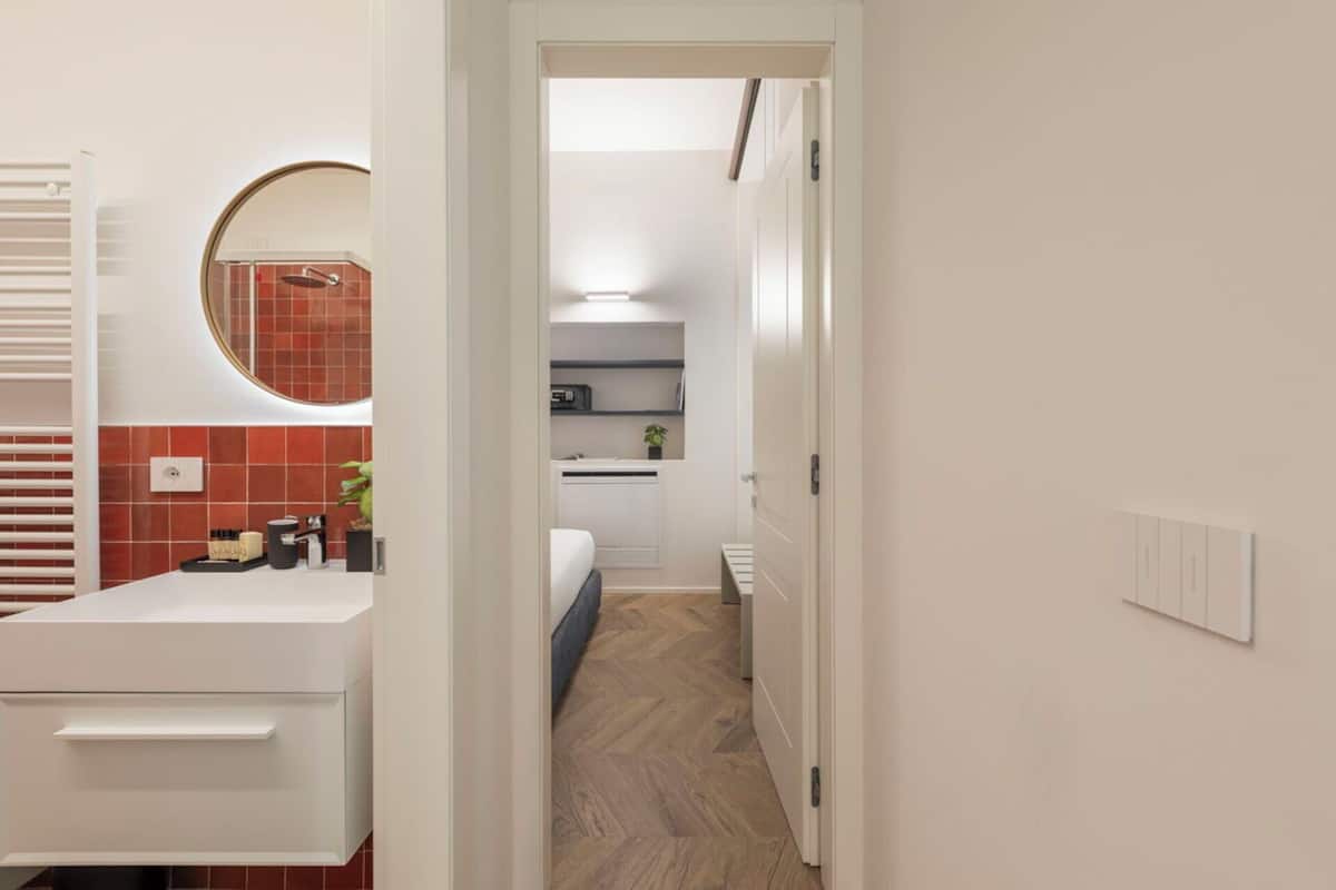 A modern bathroom with a white vanity, a round mirror, and red-tiled walls.