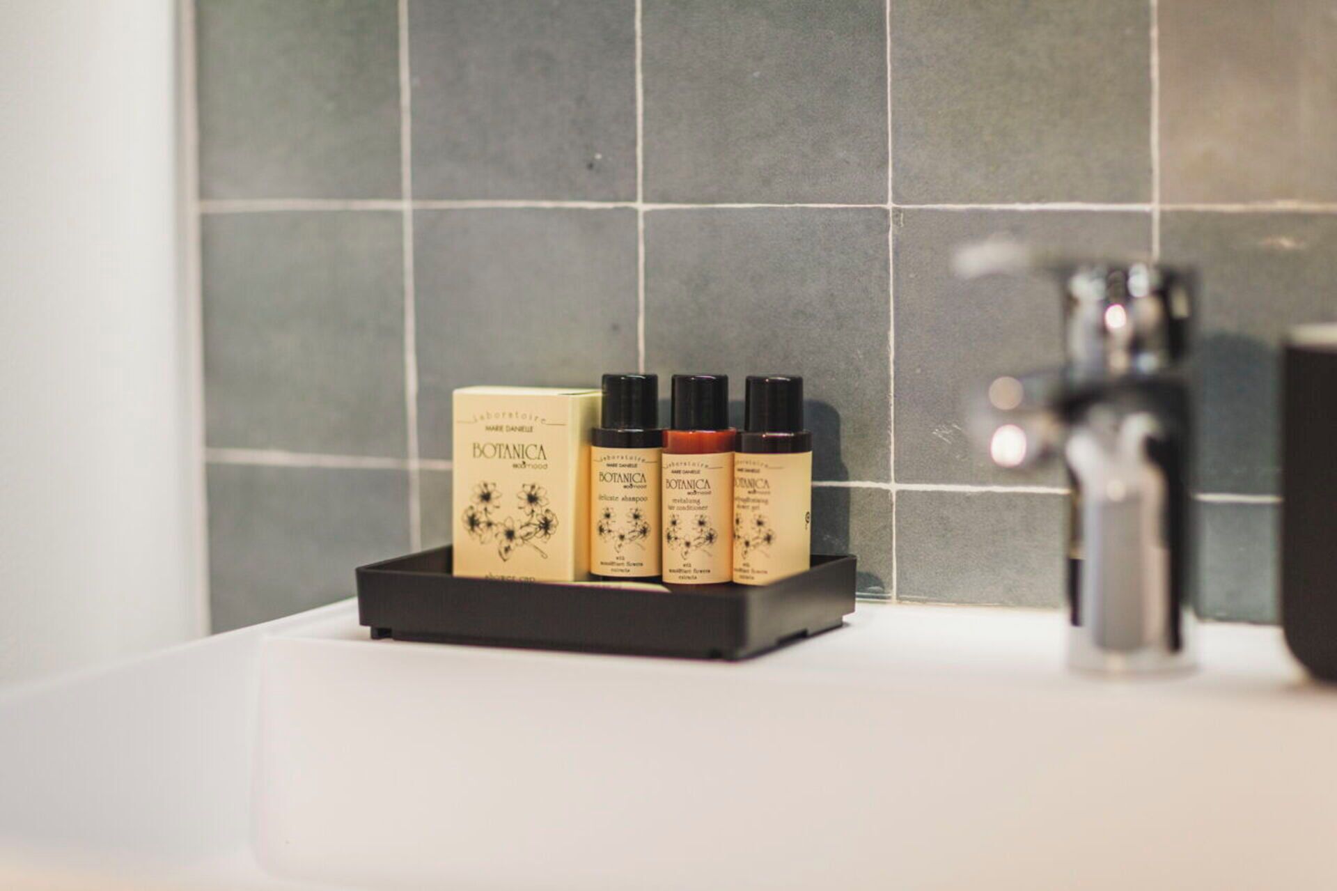 A bathroom with a black soap dish holding three bottles of Botanica body wash and a white sink.