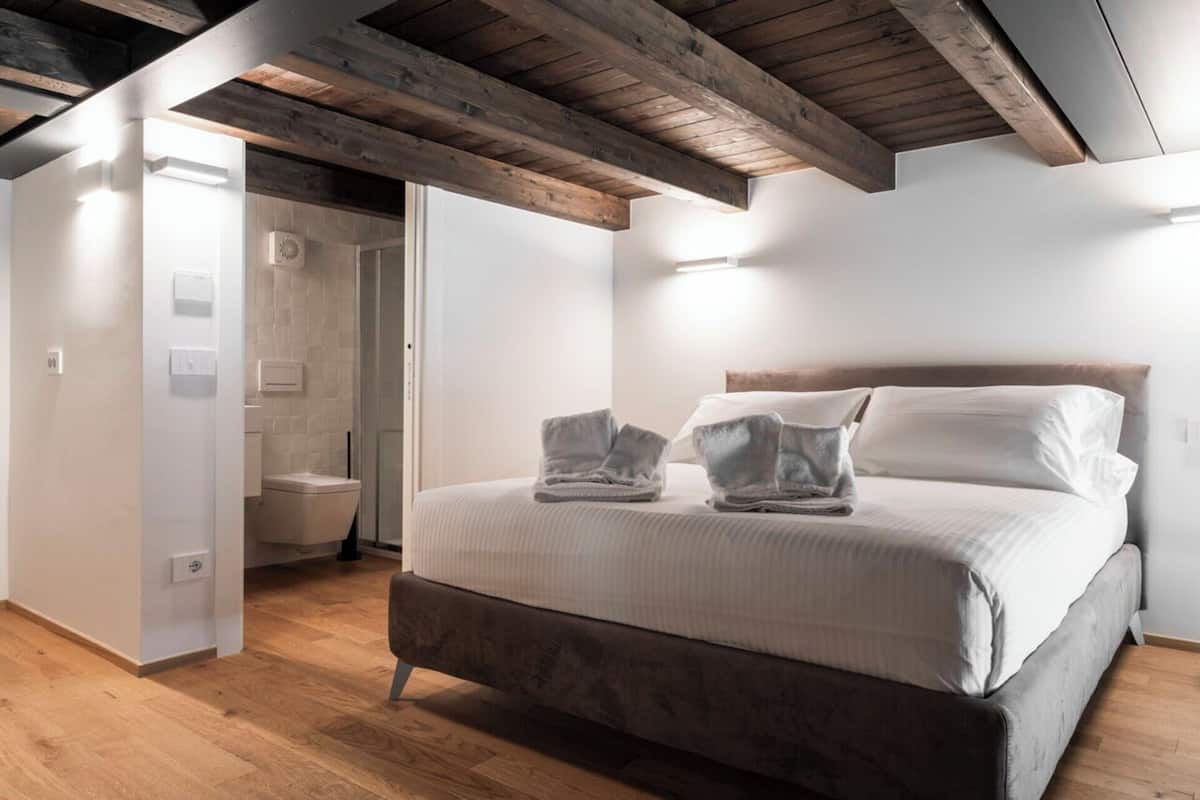 A bedroom with a bed, a wooden ceiling, and a bathroom visible through an open door.