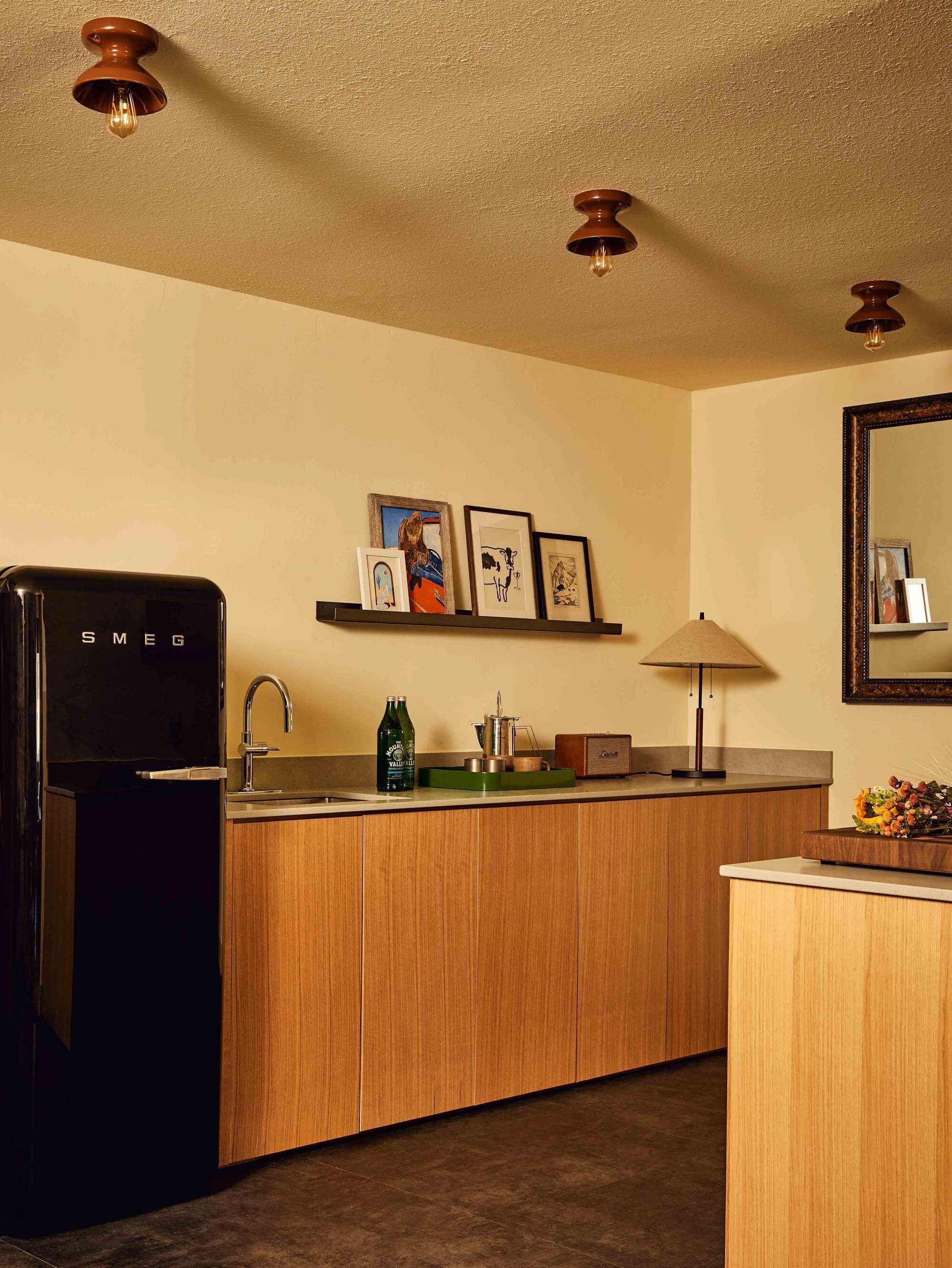 Une cuisine compacte équipée d’un réfrigérateur, d’un évier, d’un plan de travail en bois, d’un miroir et d’un ventilateur de plafond.