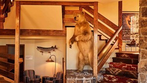 Escada de madeira com uma estátua de urso na base, um peixe fixado na parede e uma placa com detalhes sobre o evento.