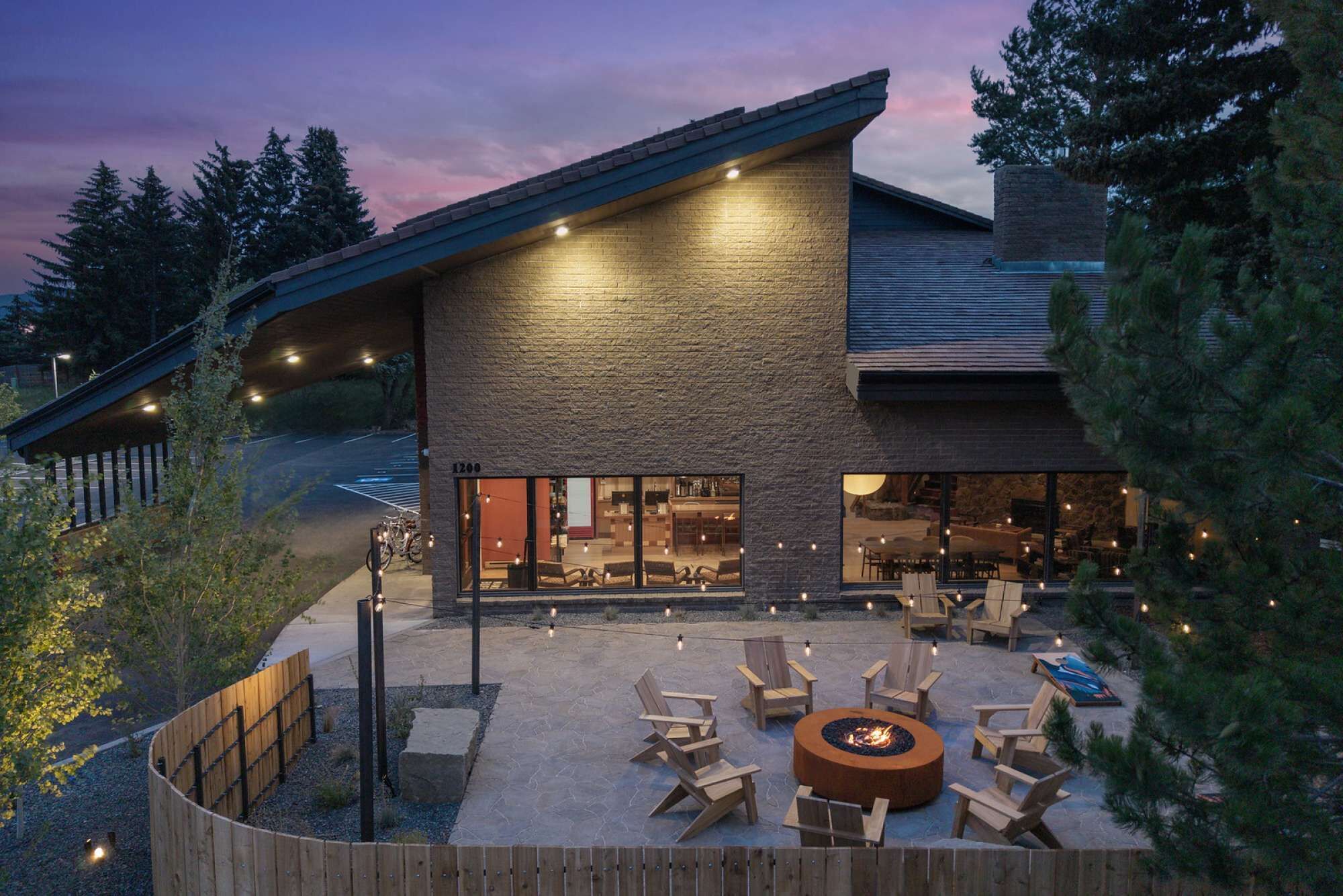 A modern building with a stone facade, large windows, and an outdoor seating area with chairs and a fire pit.