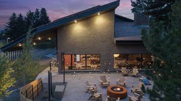 A modern building with a stone facade, large windows, and an outdoor seating area with chairs and a fire pit.