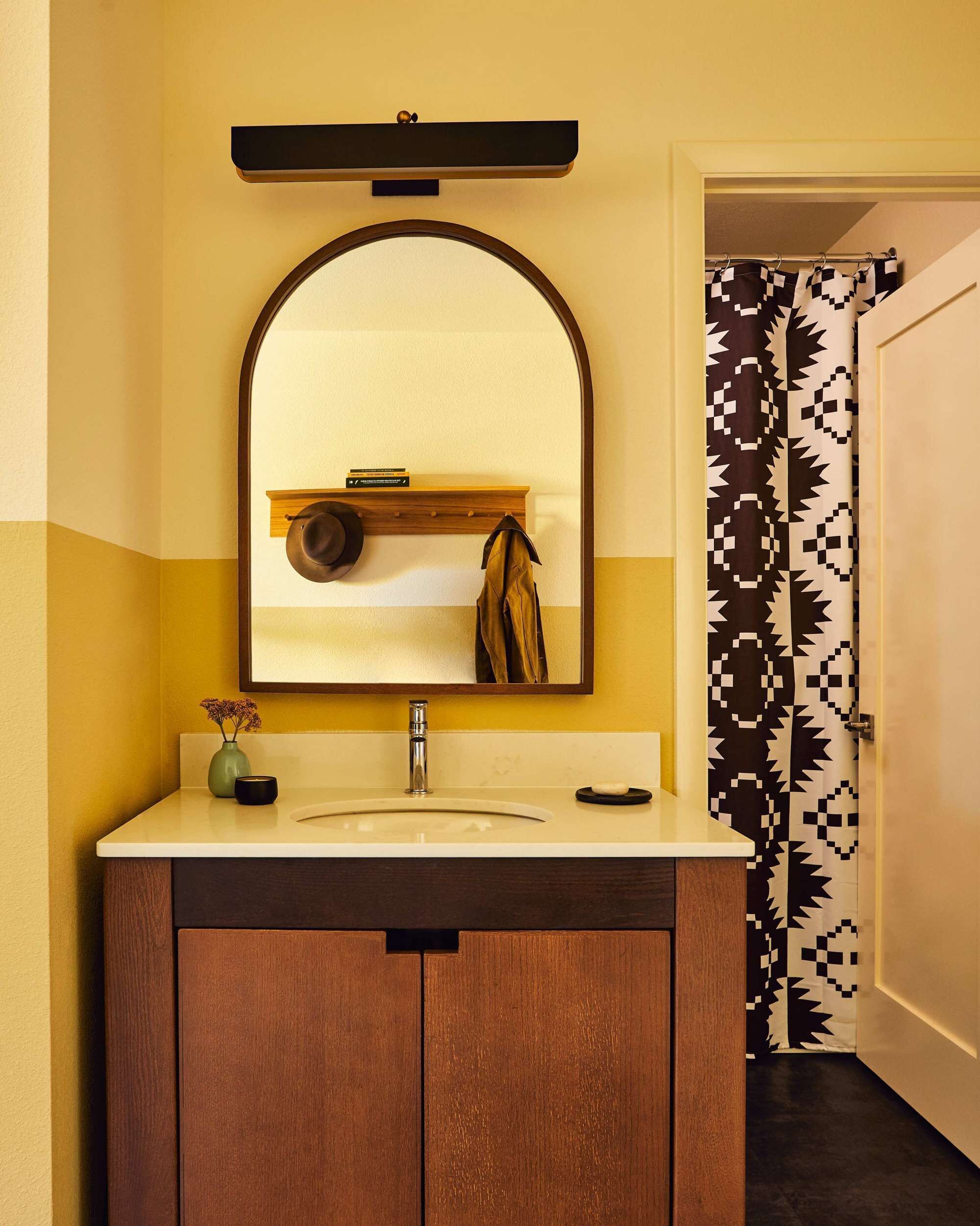 A bathroom with a wooden vanity, a mirror, and a shower curtain with a geometric pattern.