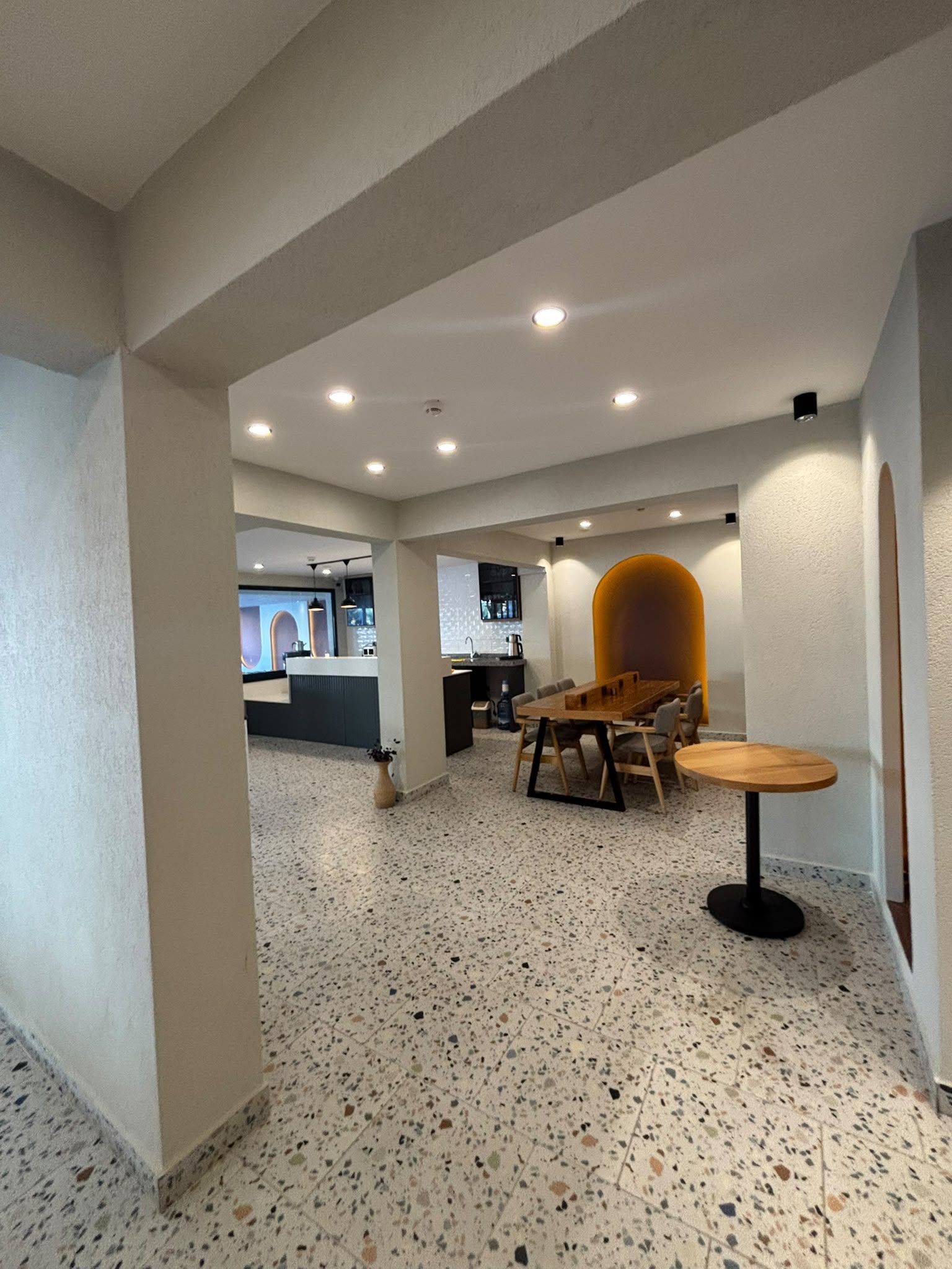 A spacious room with a kitchenette, a dining area with a table and chairs, and a large arched window.
