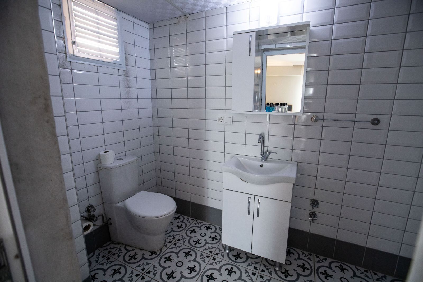 A bathroom with white tiles, a toilet, a sink, and a mirror.