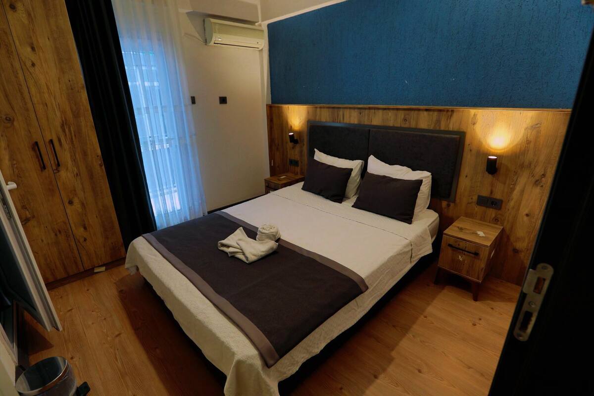 Une chambre d’hôtel avec un grand lit, une tête de lit en bois, des tables de chevet et une vue sur l’extérieur.