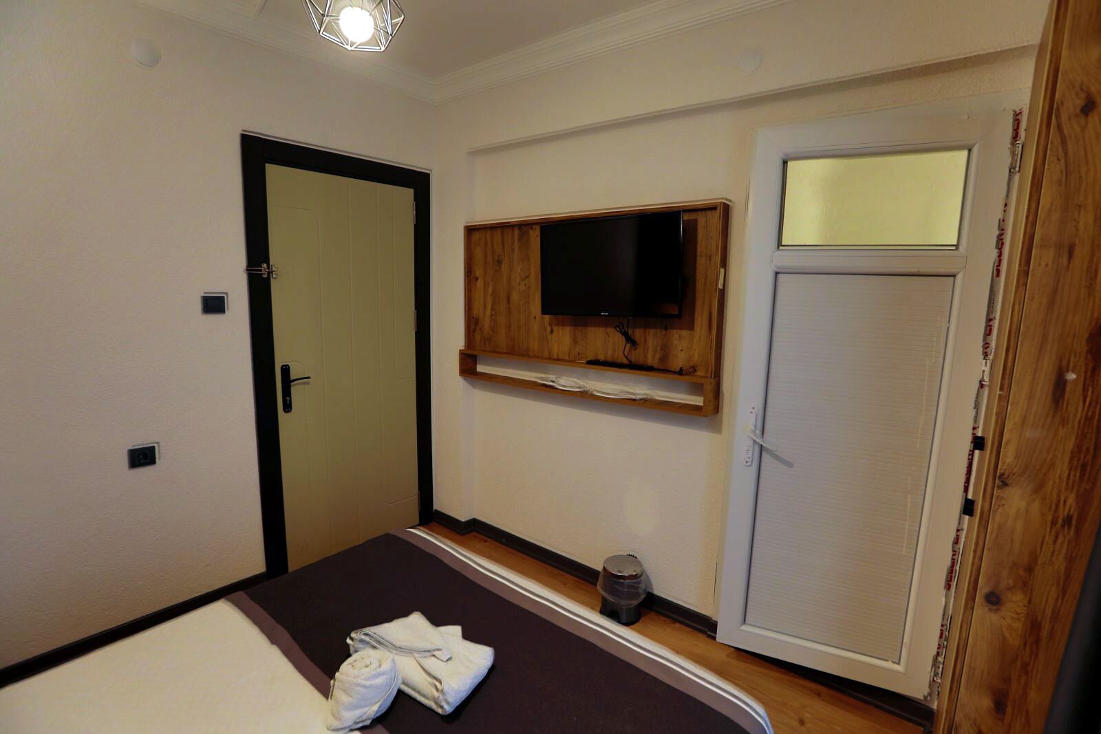 A room with a bed, a television mounted on the wall, a door, and a window.
