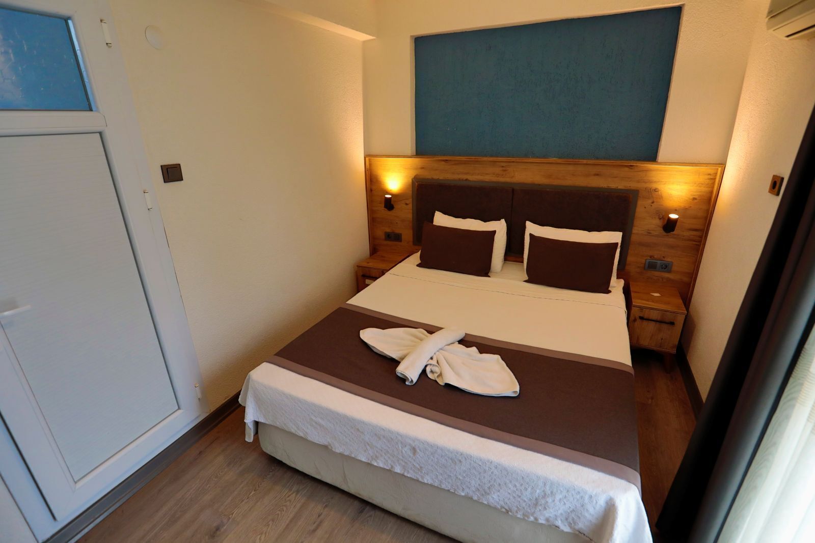 A hotel room with a bed, a wooden headboard, two bedside tables, and a window.