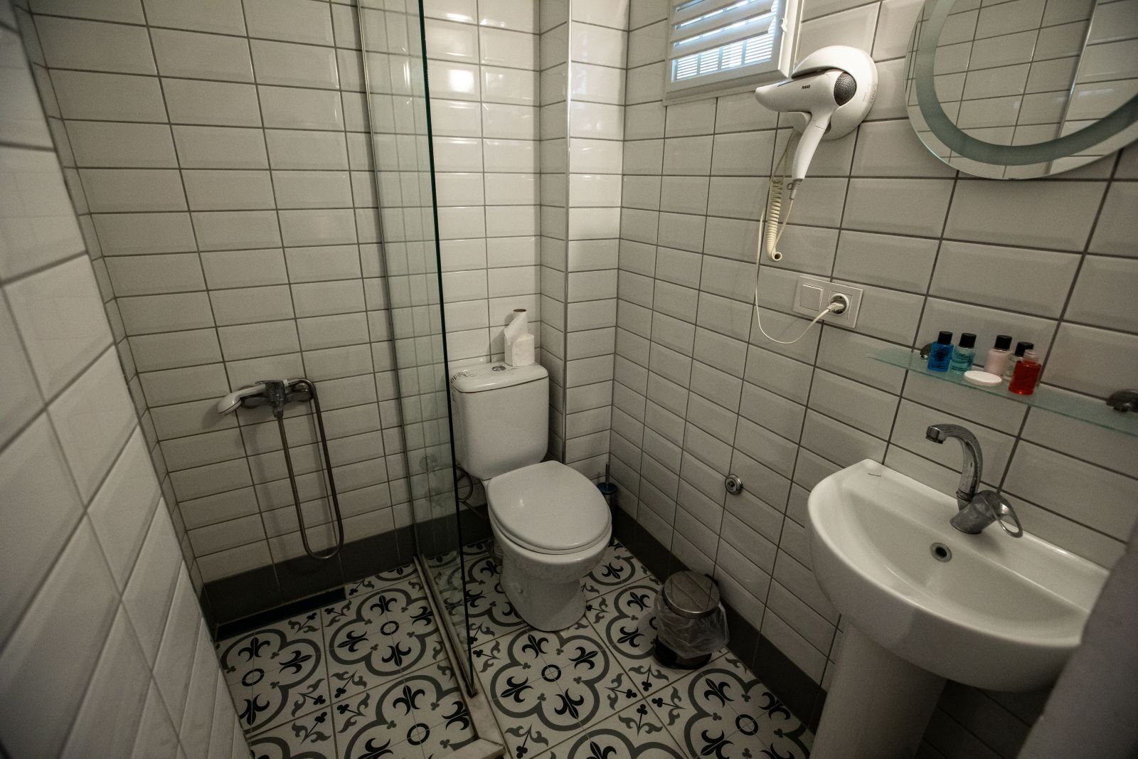 Un baño con azulejos blancos, inodoro, lavabo, secador de pelo y ducha.