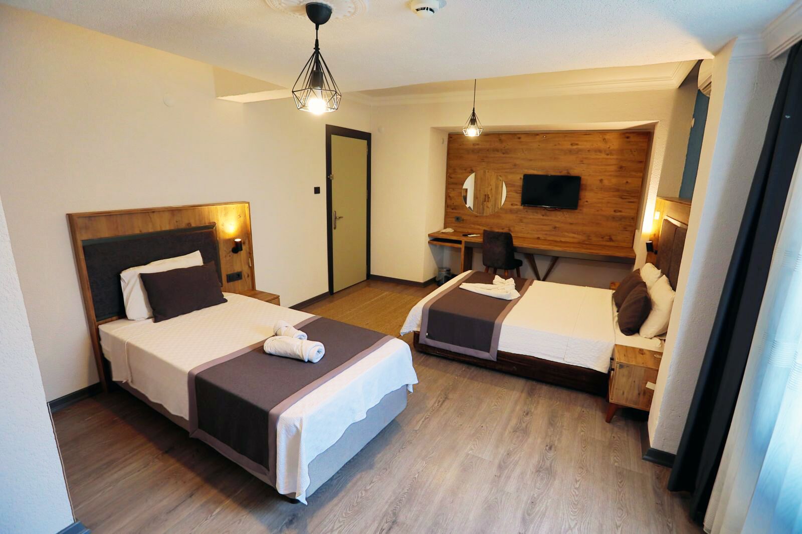 A hotel room with two beds, a desk, a chair, a TV, and a wooden accent wall.