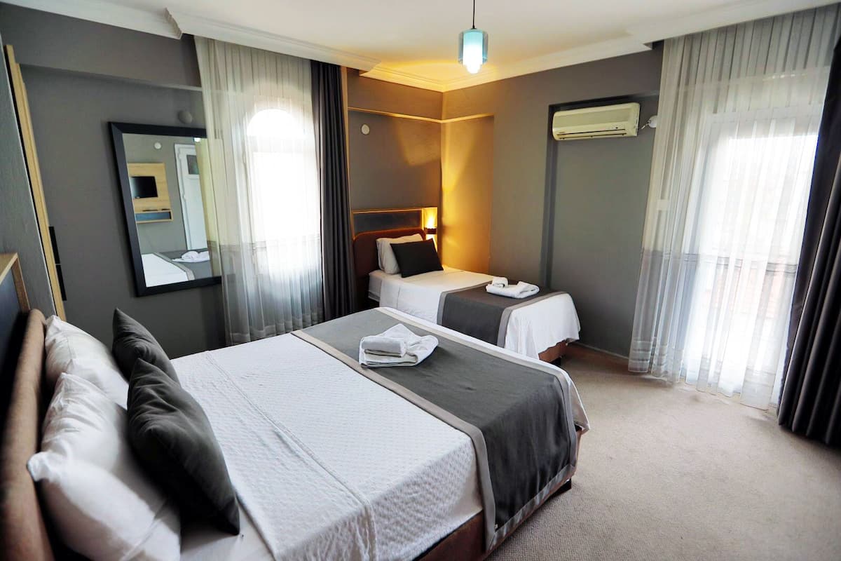 Une chambre d’hôtel avec un grand lit, un plus petit lit, un bureau, un miroir et un appareil de climatisation.