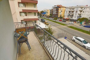 Ein Balkon mit Stuhl, Geländer und Blick auf eine Straße mit Autos und Gebäuden.