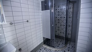 A bathroom with white tiled walls, a shower with a glass door, and patterned floor tiles. - Ida Efes Hotel (Selcuk)