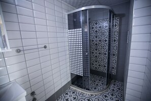 Un baño con paredes de azulejos blancos, una ducha con puerta de vidrio y baldosas de piso con diseño.