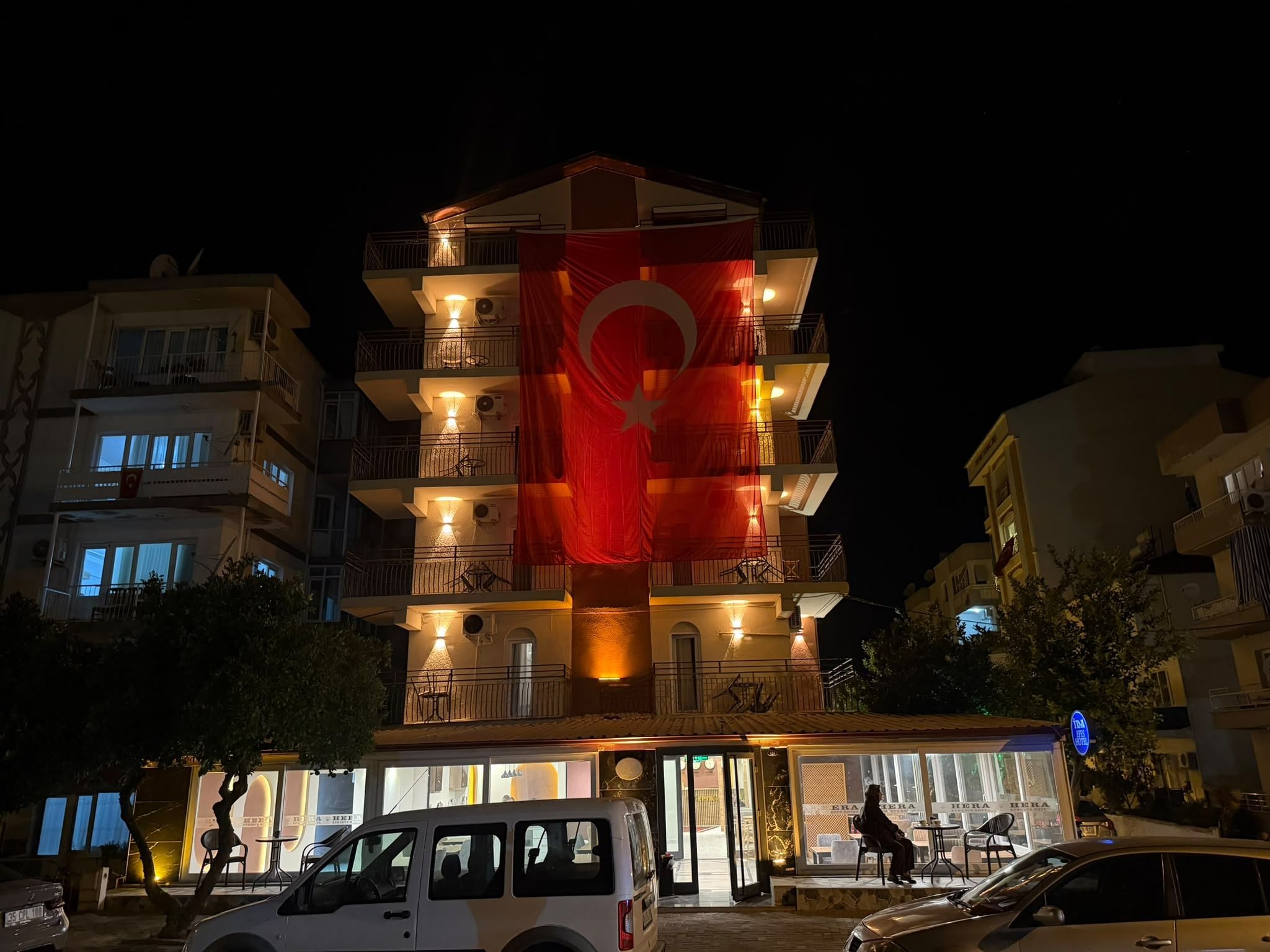 A multi-story building with balconies, a flag, and a restaurant at the ground level.