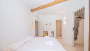 A hotel room with a bed, a wooden ceiling beam, a small table with towels, a shower area, and a door leading to another room.