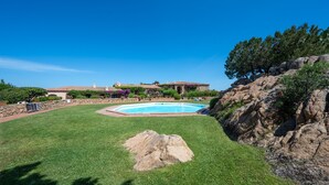 A swimming pool surrounded by a well-maintained lawn, a stone rock feature, and a building with a tiled roof.