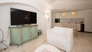 A modern living room with a flat-screen TV, a green cabinet, a white sofa, and a kitchen in the background.