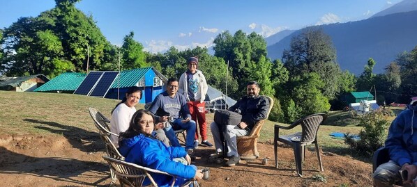A group of people sitting outdoors with solar panels and tents in the background. - Mountain Deligh Camp Chopta (Ukhimath)