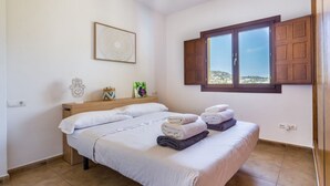 Una cama doble con toallas ordenadamente dobladas, un cabecero de madera, una obra de arte en la pared, una ventana con contraventanas de madera y vista al paisaje.