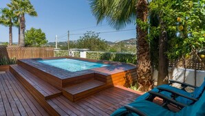 Un jacuzzi en una terraza de madera con sillas de descanso, rodeado de palmeras y vistas al paisaje.