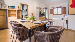 Un comedor con una mesa de madera, sillas de mimbre, un televisor y una ventana con cortinas.