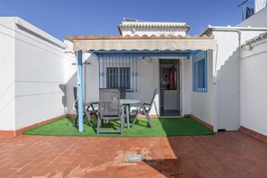 Eine Terrasse mit Tisch und Stühlen, ein kleiner überdachter Bereich und eine Tür zu einem Innenraum.