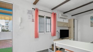 Ein Zimmer mit einem weißen Tisch, orangefarbenen Stühlen, einem Fernseher und einem Fenster mit pinkfarbenen Vorhängen.