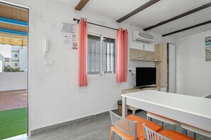 Ein Zimmer mit einem weißen Tisch, orangefarbenen Stühlen, einem Fernseher und einem Fenster mit pinkfarbenen Vorhängen.