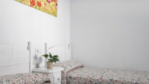 Ein Schlafzimmer mit zwei Einzelbetten, einem Nachttisch, einer Pflanze und einem Blumenbild an der Wand.