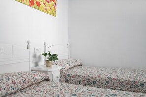 Ein Schlafzimmer mit zwei Einzelbetten, einem Nachttisch, einer Pflanze und einem Blumenbild an der Wand.