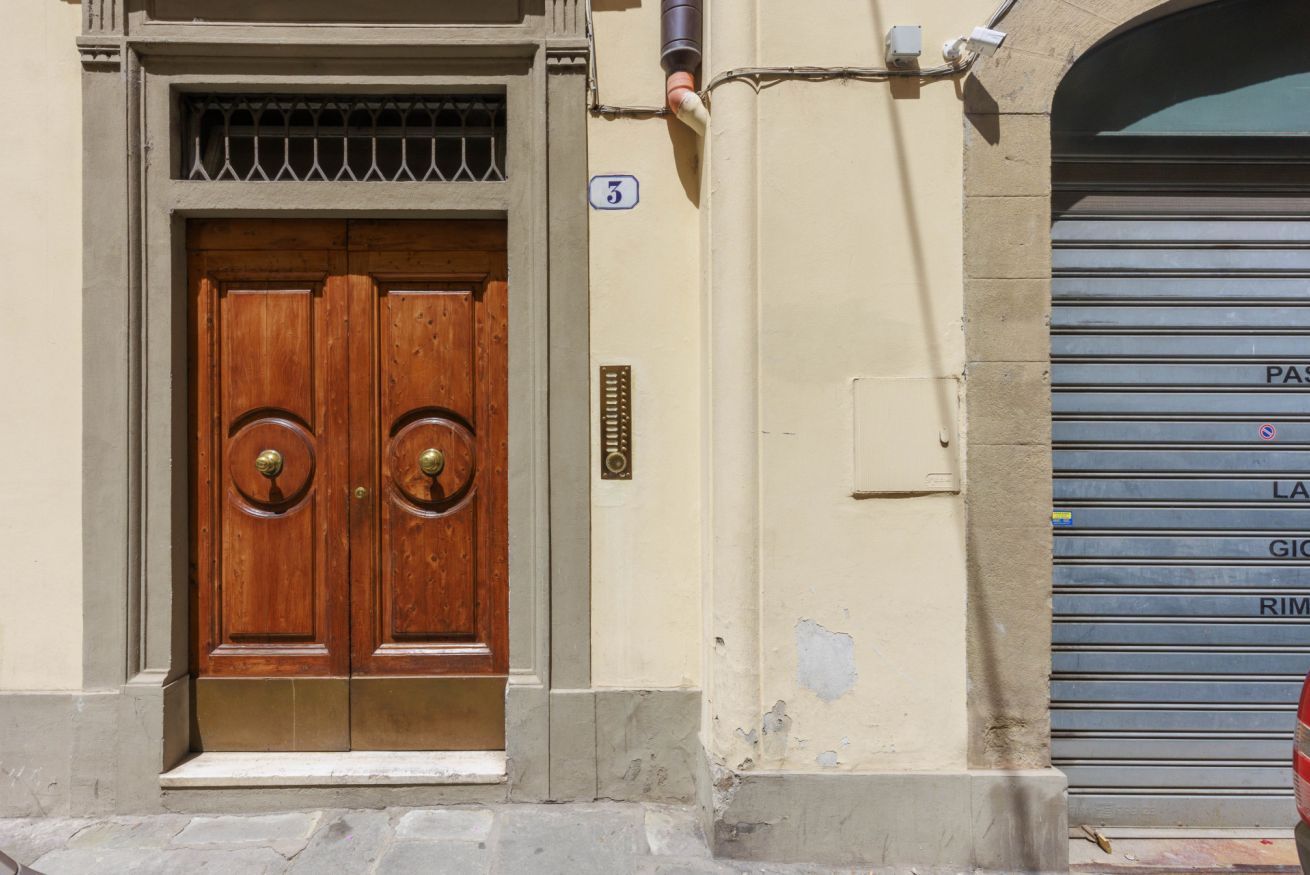 Une porte en bois à deux battants, ornée d’un heurtoir en laiton, avec un panneau indiquant le numéro « 3 » au-dessus, et une porte de garage sur la droite.
