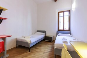 A small, clean room with two single beds, a small desk, and a chair. - Santa Maria Novella Comfort (Firenze)