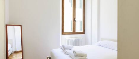 A bedroom with a bed, a window, a radiator, and a mirror.